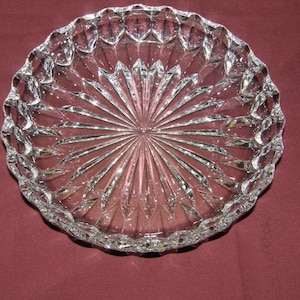 May include: A clear glass plate with a scalloped edge and a diamond-shaped pattern. The plate is on a burgundy background.