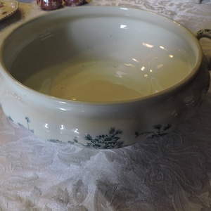 May include: A white ceramic serving bowl with two handles. The bowl features a floral pattern in green and white.