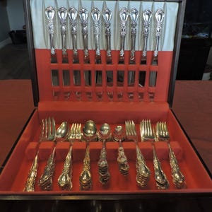 May include: A wooden box with a red velvet interior containing a set of silver cutlery. The cutlery includes forks, knives, and spoons.