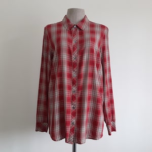 May include: A red and beige plaid button-down shirt with long sleeves, displayed on a mannequin. The shirt features a classic plaid pattern, with a mix of red, beige, and white lines creating a traditional design.
