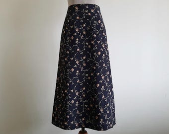 Könnte beinhalten: Ein knöchellanger Rock mit hoher Taille aus dunkelblauem Stoff, der mit einem sich wiederholenden Muster aus zarten Blumenranken mit kleinen rosa Rosenknospen und grünen Blättern bedruckt ist, präsentiert auf einem Schneiderbüsten-Torso.
