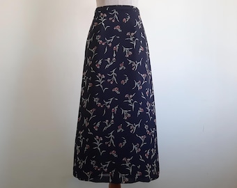 Könnte beinhalten: Ein knöchellanger Rock mit hoher Taille aus dunkelblauem Stoff, der mit einem sich wiederholenden Muster aus kleinen, gedeckten rosa Blüten mit hellgrünen Stielen und Blättern bedruckt ist. Der Rock hat eine gerade, säulenartige Form.