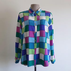 May include: A long-sleeved shirt with a vibrant checkerboard design. The shirt has a collar and buttoned cuffs. The squares are in shades of blue, green, purple, pink, and white. The buttons are gold-coloured.