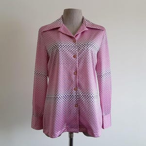 May include: Pink button-down shirt with a geometric pattern. The long-sleeved shirt has a collared neckline and is displayed on a mannequin. The pattern is a mix of pink, white, and black shapes.