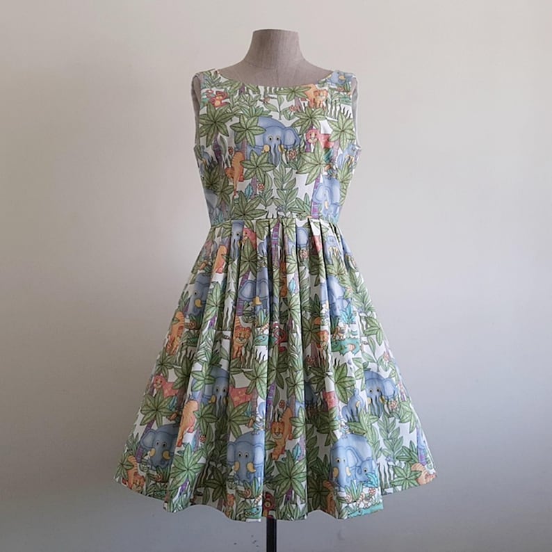 May include: A sleeveless, knee-length dress with a whimsical jungle animal print. The dress features a fitted bodice and a flared skirt. The print includes elephants, monkeys, and other animals amidst lush green foliage. The dress is displayed on a mannequin.