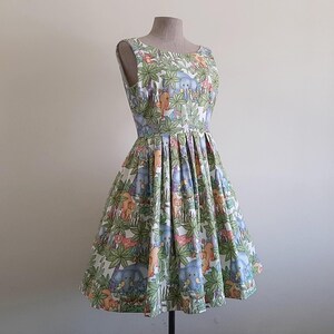 May include: A sleeveless, knee-length dress with a vibrant jungle-themed print. The fabric features elephants, lions, and other animals amidst lush green foliage. The dress has a fitted bodice and a flared skirt, displayed on a mannequin.