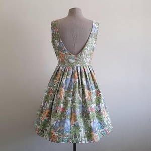 May include: A sleeveless, knee-length dress with a low back, displayed on a mannequin. The dress features a colorful jungle-themed print with elephants, giraffes, and other animals among green foliage. The skirt is pleated.