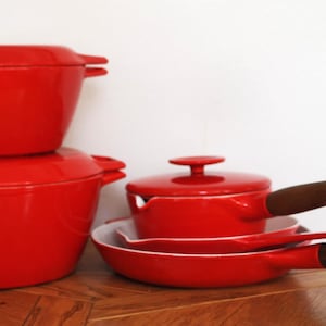May include: A set of bright red enamelled cast iron cookware including two round lidded pots, a small lidded saucepan, and a frying pan. The saucepan and frying pan feature dark brown wooden handles with silver-toned metal end caps.