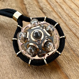 May include: A gold and silver pendant necklace with a round, geometric design. The pendant features a sphere with multiple clear glass bulbs and a black cord.
