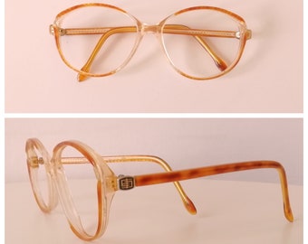 May include: A pair of tortoiseshell eyeglasses with clear lenses. The glasses have a gold-colored logo on the side.