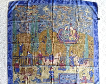 May include: Square silk scarf with a detailed illustration of a historical scene. The scarf features a blue border and a central design with figures, horses, and trees in shades of blue, green, and gold. The overall theme is a historical or cultural depiction.