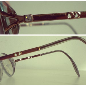 May include: A pair of gold-toned eyeglasses with a clear frame and lenses. The glasses have a double bridge and a thin metal arm.