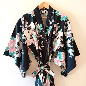 May include: A black kimono robe with a floral pattern featuring pink, white, and teal flowers and leaves. The robe has wide sleeves and a matching tie belt. The robe is hanging on a wooden hanger.