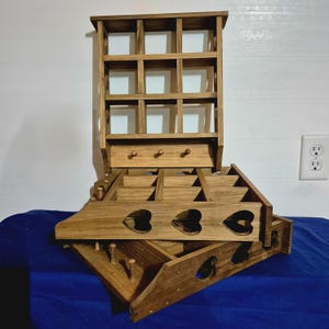 May include: A wooden shelf unit with multiple compartments and a small shelf on the top. The shelf unit is made of natural wood and has a rustic look. The shelf unit is stacked on top of a wooden box with heart-shaped cutouts.