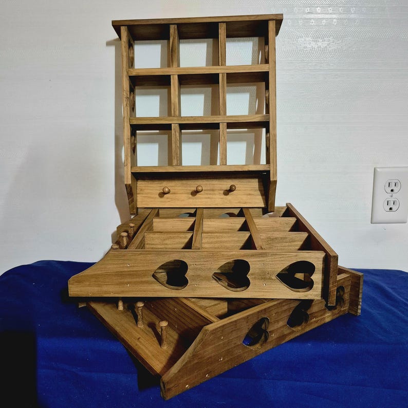 May include: A wooden shelf unit with multiple compartments and a small shelf on the top. The shelf unit is made of natural wood and has a rustic look. The shelf unit is stacked on top of a wooden box with heart-shaped cutouts.