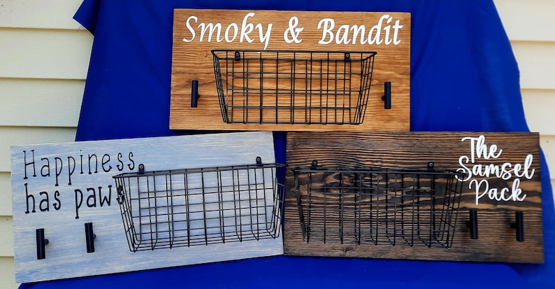 Puede incluir: Tres soportes de pared para correas de perro de madera con cestas de alambre. El soporte superior est&aacute; te&ntilde;ido de marr&oacute;n y dice "Smoky & Bandit". El soporte del medio est&aacute; pintado de azul claro y dice "Happiness has paw". El soporte inferior est&aacute; te&ntilde;ido de marr&oacute;n oscuro y dice "The Samsel Pack".