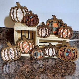 May include: A collection of eight wooden pumpkin decorations with various fall-themed patterns. The pumpkins are painted in shades of brown, orange, and red with plaid, floral, and polka dot designs.