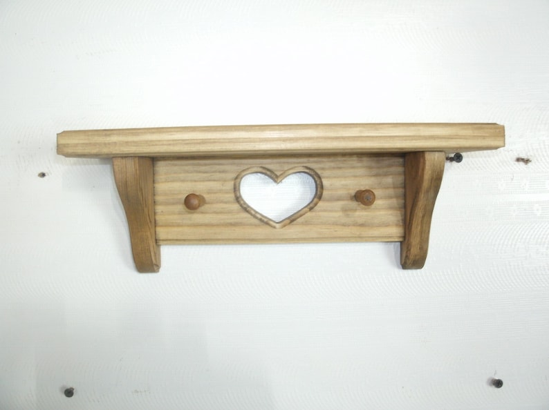 May include: Wooden shelf with a heart-shaped cutout and two small pegs. The shelf is made of light-colored wood and has a simple, rustic design. The shelf is approximately 18 inches wide.