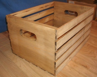 May include: A wooden crate with a natural finish and two handles. The crate has a rectangular shape and is made of wood slats.