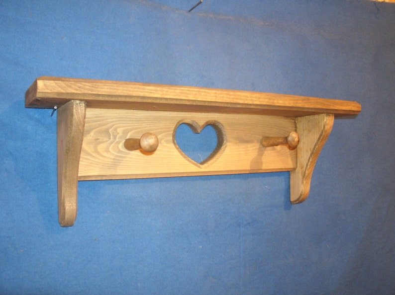 May include: Wooden shelf with a heart-shaped cutout and two wooden pegs. The shelf is made of light brown wood and has a rustic, handmade appearance. The shelf is designed for wall mounting and is suitable for displaying small items.