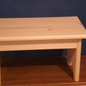 May include: A simple, wooden step stool with a light wood finish. The stool has a rectangular top and four legs.
