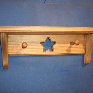 May include: A wooden shelf with two hooks and a star cutout. The shelf is stained a light brown color.