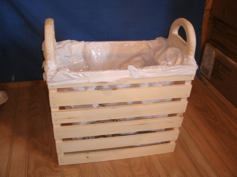 May include: A wooden crate with a plastic liner, perfect for storing items or as a trash can. The crate has a natural wood finish and is made of sturdy wood.