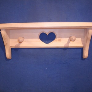 May include: A natural wood shelf with a heart-shaped cutout and two wooden knobs. The shelf is mounted on a blue wall.