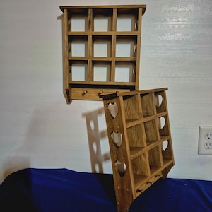 May include: Two wooden wall shelves with a rustic finish. The top shelf has a grid of 12 square compartments. The bottom shelf has a grid of 6 square compartments with heart cutouts on the sides. Both shelves have hooks on the bottom.