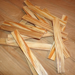 May include: A pile of thin wooden strips with a natural wood grain pattern. The strips are various shades of brown and have a slightly reddish hue.