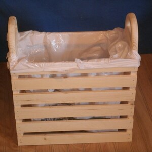 May include: A wooden crate with a white plastic liner. The crate has a handle on each side and is made of natural wood.