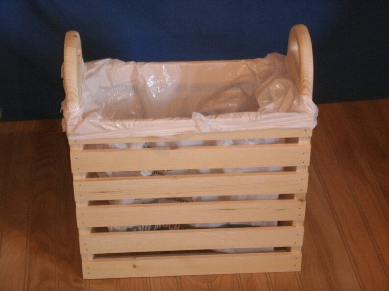 May include: A wooden crate with a white plastic liner. The crate has a handle on each side and is made of natural wood.