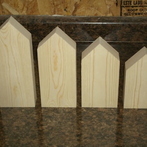 May include: Four unfinished wooden house shapes in various sizes. The houses are made of light wood and have a pointed roof.