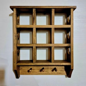 May include: A wooden wall shelf with 12 square compartments and three hooks on the bottom. The shelf is stained a dark brown color.