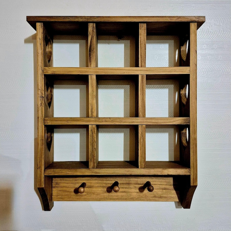 May include: A wooden wall shelf with 12 square compartments and three hooks on the bottom. The shelf is stained a dark brown color.