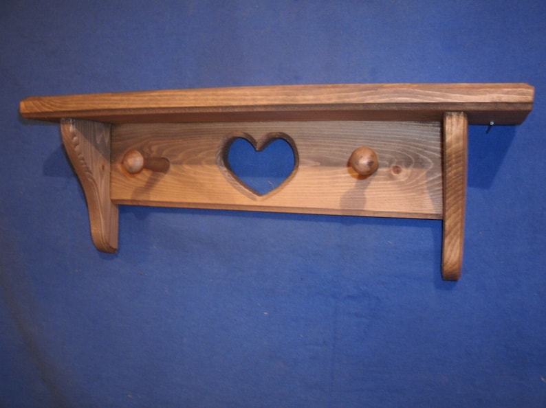 May include: A wooden shelf with a heart-shaped cutout and two wooden knobs. The shelf is made of light brown wood and has a rustic, handcrafted appearance. It is designed for wall mounting and has a simple, functional design.