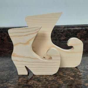 May include: Two unfinished wooden elf shoes. The shoes are made of light wood and have a simple design. They are perfect for crafting and decorating.