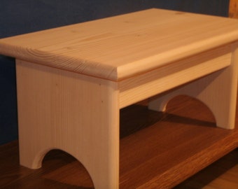 May include: A natural wood step stool with rounded edges and arched legs. The stool is made of unfinished wood and is ready to be painted or stained.