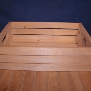 Peut inclure: Une caisse en bois naturel de forme rectangulaire et de couleur brun clair. La caisse a une poign&eacute;e de chaque c&ocirc;t&eacute; et est en bois brut.