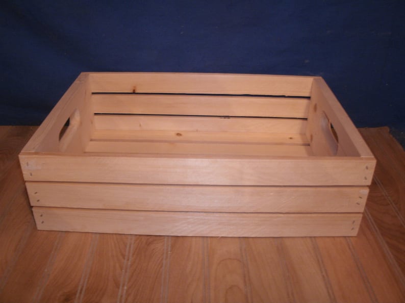 Peut inclure: Une caisse en bois naturel de forme rectangulaire et de couleur brun clair. La caisse a une poign&eacute;e de chaque c&ocirc;t&eacute; et est en bois brut.