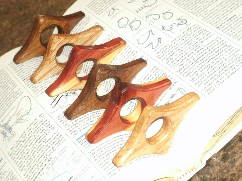 Puede incluir: Cinco sujetalibros de madera en varios tonos de marr&oacute;n, rojo y amarillo. Los sujetalibros tienen forma de diamante con un agujero redondo en el centro.
