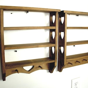 May include: Two matching brown wooden wall shelves featuring three horizontal tiers and a bottom rail with three small pegs. The side panels are decorated with cut-out heart shapes, and the bottom center piece also features a heart-shaped cut-out.