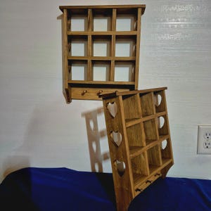 May include: Two wooden wall shelves with a rustic finish. The top shelf has a grid of nine square compartments. The bottom shelf has a heart-shaped cutout design and three hooks.