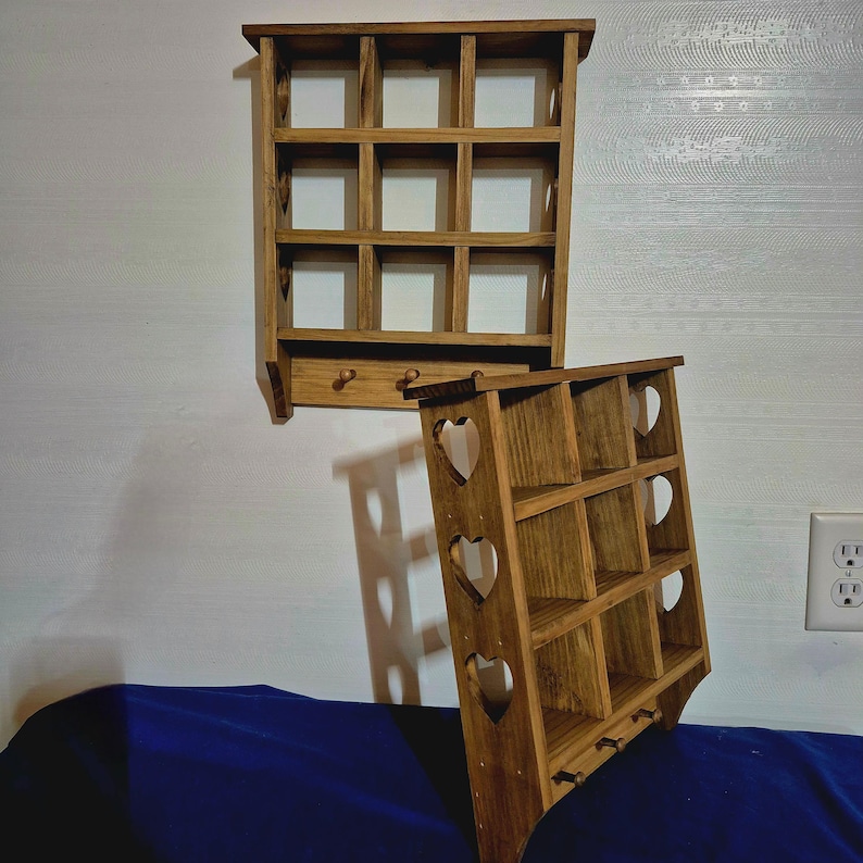 May include: Two wooden wall shelves with a rustic finish. The top shelf has a grid of nine square compartments. The bottom shelf has a heart-shaped cutout design and three hooks.