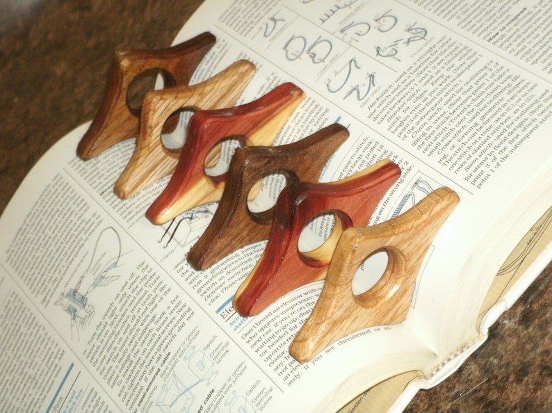 Puede incluir: Cinco sujetalibros de madera en varios tonos de marr&oacute;n, rojo y madera natural. Cada sujetalibros tiene forma de tri&aacute;ngulo con un agujero redondo en el centro.