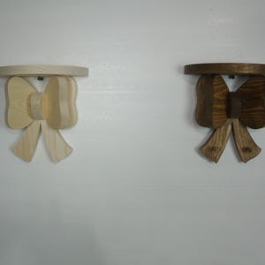 May include: Two wooden bow-shaped shelves. One is natural wood, the other is stained brown. Each shelf has a round top and a bow-shaped support. The shelves are mounted on a white wall.