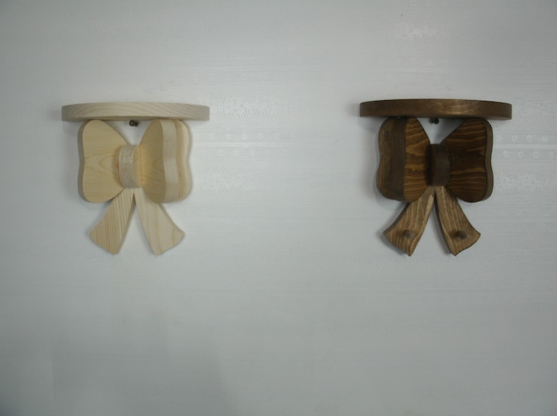 May include: Two wooden bow-shaped shelves. One is natural wood, the other is stained brown. Each shelf has a round top and a bow-shaped support. The shelves are mounted on a white wall.