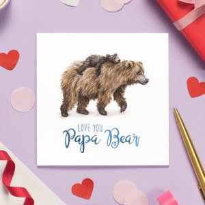 Peut inclure: Une carte blanche avec une illustration aquarelle d'un ours brun avec un petit ourson brun mont&eacute; sur son dos. Le texte "Love you Papa Bear" est &eacute;crit en bleu sous les ours.