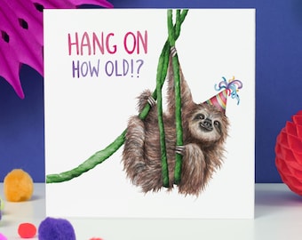 May include: A square greeting card featuring a watercolor illustration of a sloth hanging from a green vine. The sloth wears a party hat. The text "HANG ON HOW OLD!?" is written in pink and purple.