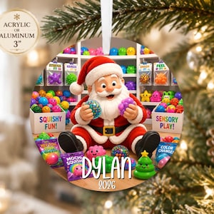 May include: A 3-inch round acrylic or aluminum ornament featuring a cartoon Santa Claus surrounded by colorful sensory toys. The image includes text reading SQUISHY FUN, SENSORY PLAY, NEEL DOH, MOCHI SQUISHY, DYLAN, and 2026, with a white ribbon for hanging.